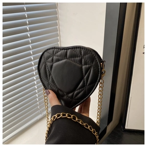 Detail of a black heart-shaped quilted leather bag featuring a gold metal chain strap