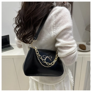 Detail of black shoulder bag featuring gold bow hardware and elegant chain handle