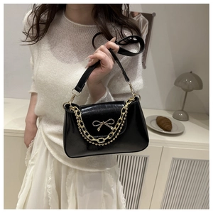 Detail of black glossy handbag featuring golden bow clasp and stylish double chain straps
