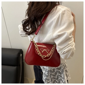 Detail of red patent leather shoulder bag featuring a gold metal bow and dual chain straps