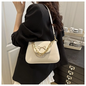 Detail view of cream white shoulder bag featuring a metallic bow and chain strap