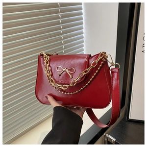 Detail of wine red leather underarm bag featuring a golden bow buckle and chain tassels