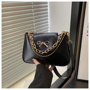 Detail of black faux leather bag with gold bow clasp and decorative metal chains