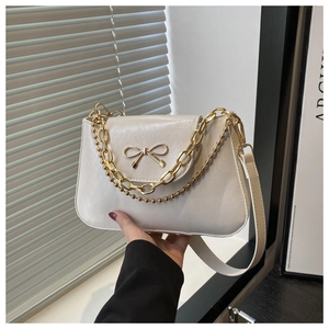 Close-up of cream shoulder bag with golden bow hardware and textured leather finish