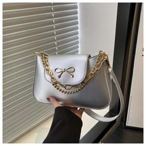 Detailed close-up of a silver matte bag featuring a gold bow and metallic chain strap
