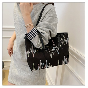 Close-up of black tote bag featuring colorful wavy embroidery and faux leather handles