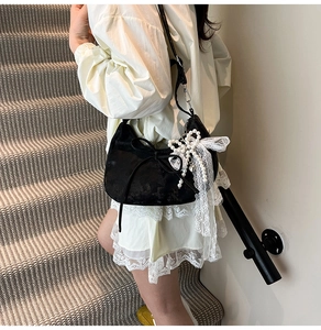 Detail of black crescent bag with lace bow, pearls, and texture on a female model