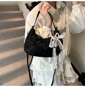 Detail of black velvet half-moon bag with bow decoration and pearl lace charm