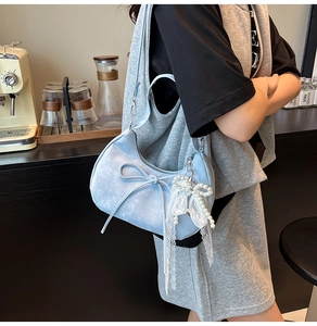 Detail of light blue crescent bag with bow decoration and pearl lace charm in a cafe