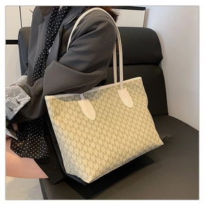 Detail of large tote bag with repetitive M pattern and double shoulder straps on sofa