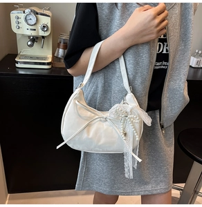 Detail of white crescent bag with bow decoration and pearl lace heart charm pendant