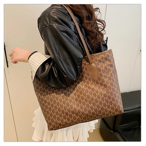 Detail of a brown tote bag with M letter print and slender shoulder straps
