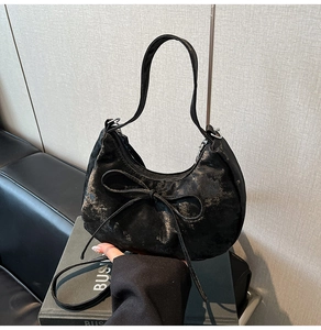 Detail view of black crescent bag with vintage metallic texture and bow tie buckle decoration