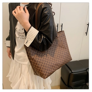 Detail view of a large brown tote bag with all-over M-pattern print and leather straps