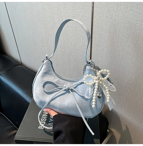 Detail of light blue crescent bag with velvet finish, satin bow and pearl pendant