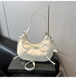 Detail of off-white crescent bag featuring a delicate leather bow and metallic hooks