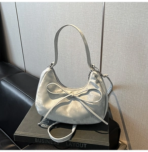 Detailed view of a silver-grey crescent bag with a delicate bow on a velvet fabric finish