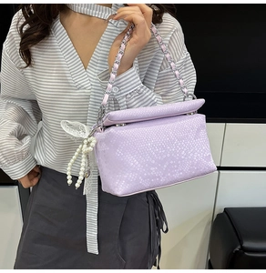 Close-up of light purple snakeskin texture handbag with pearl and lace bow charm