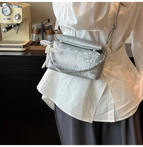 Detail of silver snake-pattern box bag with elegant pearl and lace charm accessories