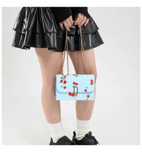 Detail of light blue saddle bag featuring cherry print, gold chain, and cute charm