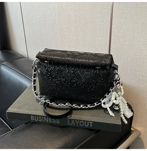 Detail of black snakeskin texture bag with pearl ribbon charm and silver chain strap