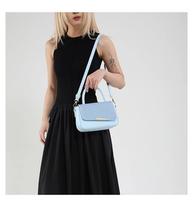 Close-up of a light blue crossbody bag with woven texture flap and gold hardware trim