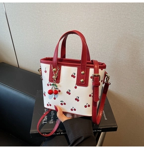 Détail du sac seau à imprimé cerises avec poignées rouges et un charmant pendentif 3D