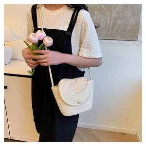 Detail of cream woven shoulder bag with spiral flap design and decorative pearl accent