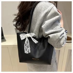 Detalle de bolso tote negro con gran lazo de encaje blanco y letras doradas de moda