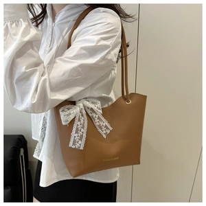 Detalle de bolso tote de cuero marrón con lazo de encaje blanco y texto grabado