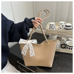 Detalle de bolso tote de cuero beige con lazo de encaje blanco y letras doradas