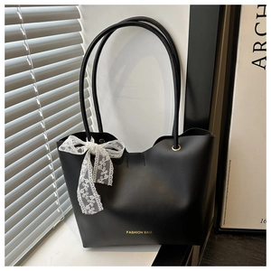 Detalle de bolso tote de cuero negro con letras doradas y accesorio de lazo de encaje blanco