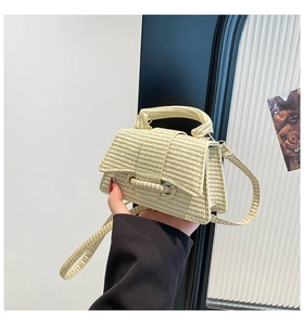 Detail of beige woven mini straw handbag with flap closure and matching strap handle