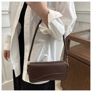 Model wearing dark brown leather underarm bag with minimalist curved flap and gold hardware