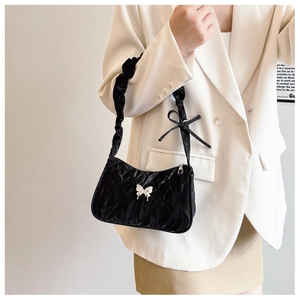 Detail of black pleated shoulder bag with silver butterfly emblem and satin bow strap