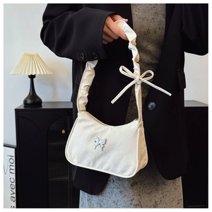 Détail du sac bandoulière crème avec fermoir papillon argenté et bandoulière plissée