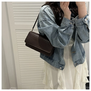 Detail of dark brown woven leather baguette bag showing texture on casual outfit