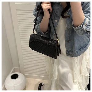 Close-up of black woven shoulder bag with golden hardware on a denim jacket model