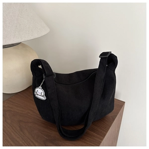 Detail of black corduroy dumpling bag with adjustable strap and cute cartoon puppy charm