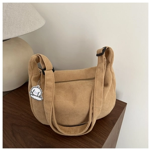 Detail of beige corduroy hobo bag with adjustable black strap and cute puppy pendant