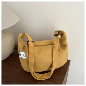 Detail of yellow corduroy tote bag featuring adjustable strap and white dog charm