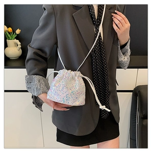 Gros plan d'un sac seau blanc à paillettes porté sur un blazer gris avec foulard en soie