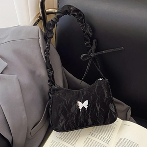 Sac sous le bras froncé noir avec papillon argenté sur fond de studio minimaliste