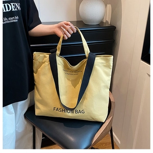 Detail of yellow canvas tote bag with black handles and fashion lettering on black chair