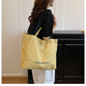 Side view of model wearing a large yellow canvas tote bag with black letter print