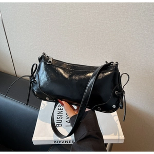 Detail of black glossy leather shoulder bag with silver rivets and decorative side bows