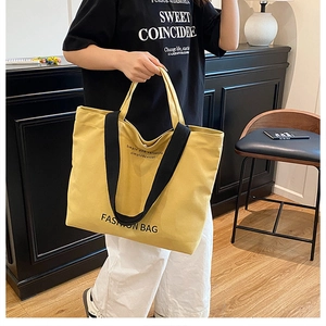 Detail of a large yellow canvas tote bag with black straps and fashion lettering
