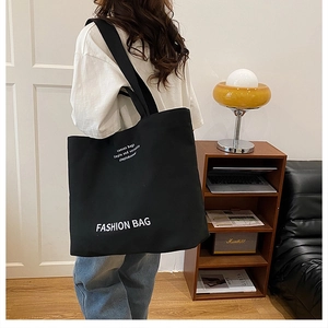 Close-up of black canvas tote bag with white lettering and thick shoulder strap detail