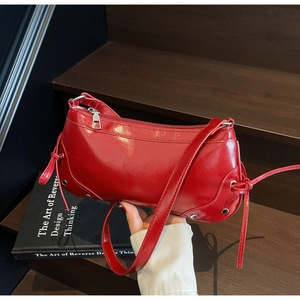 Detail of red patent leather shoulder bag featuring metallic studs and long leather tassels