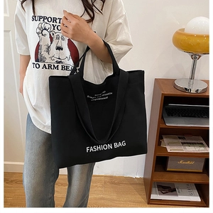 Detail of a black canvas tote bag with fashion typography worn by a model in a cozy room